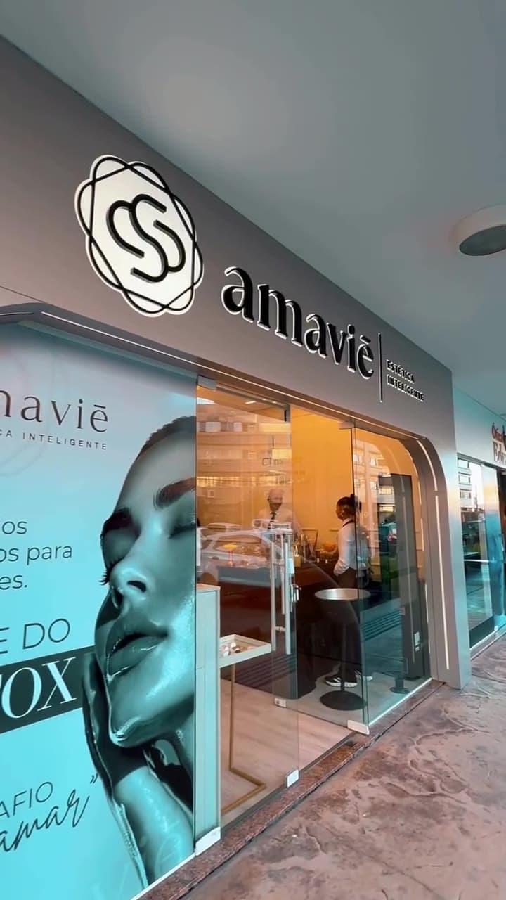 Fachada da clínica Amaviē Estética Inteligente, com o monograma e o letreiro iluminados, em Kobrasol, São José/SC